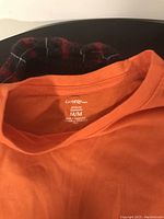 Close-up of the neck collar of the orange T-shirt showing George brand label and size M/M.