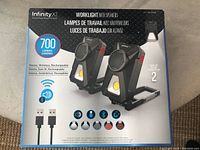 Front of the box showing the Infinity XT wireless work light with speakers, 700 lumens, stereo wireless rechargeable features, and image of two units with USB cables.