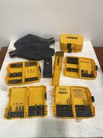 Photo showing all Dewalt tool accessories including yellow bit cases with bits, two empty yellow cases, black rubber dust collection bags, yellow bit holder and metal bit holder attachment.