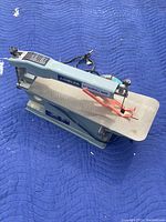 Side view of Delta 15-inch scroll saw on blue padded surface showing the upper arm and table.