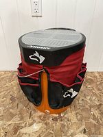 Front view of red and black Husky tool bucket cover insert fitted over an orange 5 gallon bucket with black lid, showing multiple tool pockets and Husky logos.