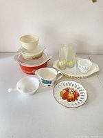 Vintage kitchen dishes lot with two images showing various Pyrex glass and ceramic dishes with lids, glass tumblers, cups, bowls, and plates in mixed condition including some chips in lids.