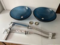 Two blue glass sinks, two chrome faucets, and two metal ring risers arranged on table