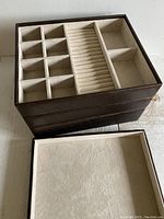 Top view of open jewelry box showing interior cream compartments including ring slots and multiple small and medium square sections.