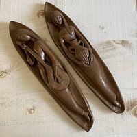 Two vintage chalkware muses sculptures with minor wear, shown lying flat on a pale wooden floor.