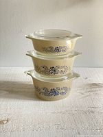 Three stacked Pyrex casserole dishes showing the blue homestead pattern on cream background.