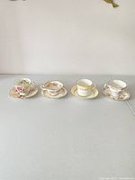 Four vintage teacups and saucers displayed showing various floral patterns and gold accents.