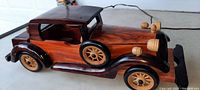 Left side and front angle view of the wooden antique car model showing details including wheels, headlights, side spare tire, and wooden roof.