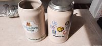 Front view of two heavy stoneware beer mugs; one with applied Schwaben Bräu label, the other with a pewter lid and Münchener Bier logos.