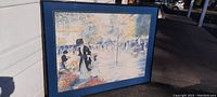 Full view of framed artwork print leaning against a wall outside, showing entire artwork and frame.