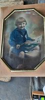 Full view of the framed photo showing child in sailor outfit holding a book, original frame with decorative gold trim and domed glass.