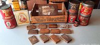 Antique country store containers arranged behind flat wooden blocks including King Syrup cans, Heyl's Syrup can, Norton Bros. Mustard tin, and wooden crate.