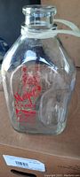 Front view of the clear glass gallon milk bottle showing red Meyer Dairy logo and farm scene, with plastic strap around the neck.