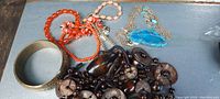 Photo showing several costume jewelry items including heavy brown bead necklace, orange and pink bead bracelets, gold-tone bangle, and blue stone necklace.
