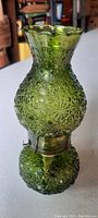 Front view of the green glass kerosene lamp with floral starburst pattern and scalloped top edge.