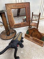 The full lot includes the advertising mirror showing company name and shoe related text, the black boot jack with textured center, the metal candle holder, the miniature woven-seated wooden chair, and the wooden house souvenir.
