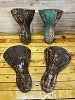 Four cast iron antique claw feet displayed on wooden surface with visible rust and chipping paint.