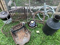 Overview showing ceramic crock, bean pot, milk jug, rusty metal tools and wire racks on grass outside barn area.