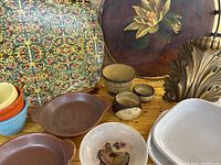 Photo showing an assortment of pottery dishes, Georges Briard floral round tray, multicolored patterned tray, brass decorative piece, and small pottery vessels.