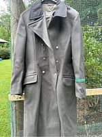 Full front view of the grey wool coat hanging outdoors showing buttons and pocket details.