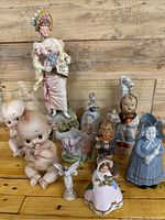 Full view of entire collection showing tall woman figurine, Kewpie dolls, Hummel figure and other small figurines