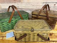 Three metal picnic baskets grouped together showing the plaid painted woven pattern and wood handles.