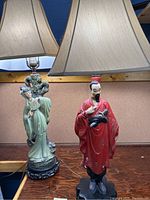 Pair of two Asian chalkware lamps on a wooden surface against a wall, showing detailed figures and lampshades