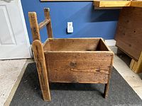 Side view of the primitive wooden box showing one long side and one end with tall vertical wooden handle/support pieces.