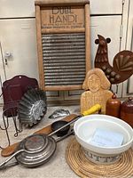 Photo showing all items in the lot arranged on a table, including the wooden-framed washboard, ceramic butter crock, wooden cutting board with carving, metal turkey decoration, red match holder, ceramic shakers, and various kitchen utensils.