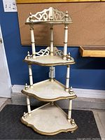 Front view of wooden corner shelf showing four tiers with ornate cutouts and brushed gold trim.