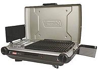 Closed Coleman 2 burner camp stove and grill with beige hinged lid, black body, two knob controls, foldable wind shields on sides, and grill grates visible inside.