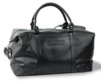 Black vegan leather weekender bag by Michel Germain with visible front logo tag, rounded handles, and silver zipper. Shown from a side-angle view highlighting the shape and hardware.