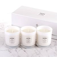 Three white scented candles in frosted glass containers with white Michel labels and a white box in the background on a marble surface.