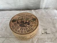 Round decorative wooden holder with printed French country artwork and text reading 'Brie Baker Rechaud a Brie','Petite Maison','IR 18','Brie Reigns Supreme','Treats were made Brie the people's cheese'. The wooden box is about 3 inches high and 7.5 inches diameter.