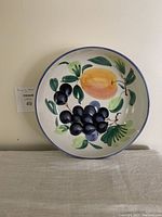 Front view of the handmade Pizzato Italian serving bowl showing fruit design including grapes and a peach with green leaves.