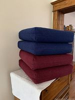 Four sofa cushions stacked, two navy blue on top and two burgundy on bottom, showing color and thickness.