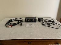Phono pre-amp device and included cables laid out on a table, shown from a distance to illustrate all included items.
