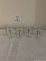 Front view of 9 clear glass sherry/liqueur glasses arranged in 3 rows on a table with white cloth.