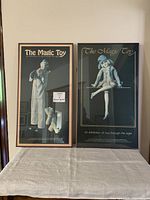 Two framed prints titled 'The Magic Toy' standing side by side on a table, showing front view of the full prints in frames.