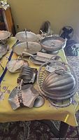 Photo showing multiple aluminum serving ware items including tiered trays, bowls, dome-covered butter dish, and other small dishes on a yellow tablecloth.