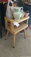 Mid century modern tiered side table with decorative vases on top, showing front and part of left side.