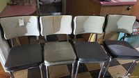 Front view of four vintage vinyl padded kitchen chairs with chrome frames lined up side by side, showing wear on seats and backs.