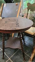 Full view of the vintage wooden round side table showing top surface wear, turned legs, and lower shelf.