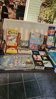 Photo showing multiple vintage boxed games including Bingo, Cootie, Dominoes, Flinch, Tinker Toys, and others on a table.