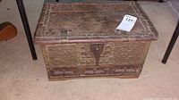 Full view of the rectangular wooden box showing carved design and metal studs with front drawers and locking latch.