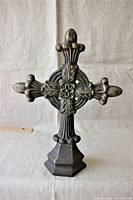Full view of ornate cast metal cross on fabric background showing front details and hexagonal base