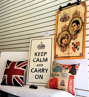 Photo shows Irish Linen banner with portraits of Prince Charles and Princess Diana, Union Jack cushion, British icon cushion, Keep Calm and Carry On wooden wall plaque, and small black model car.
