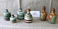 Full view of two separate handmade ceramic condiment sets with lids and cork stoppers placed on fabric background