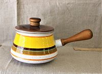Side view of the yellow enameled pot with wooden handle and lid knob on a fabric background.