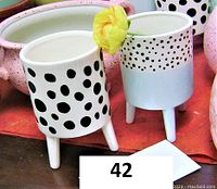 Two white ceramic planters on legs with black polka dot patterns, one with larger dots and one with smaller dots on upper half.